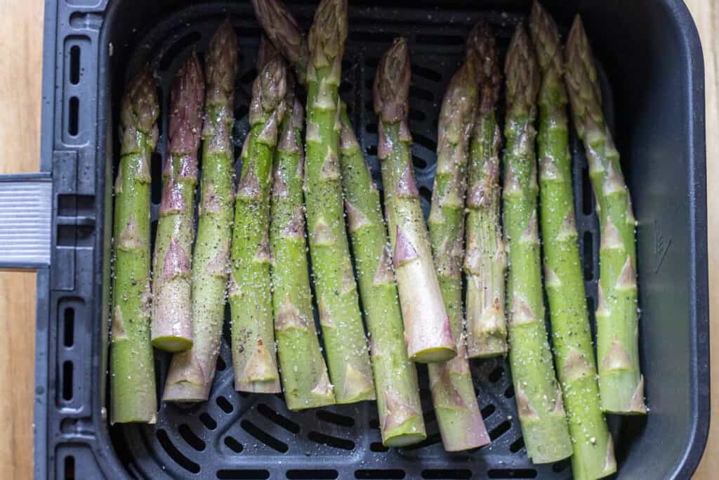 seasoned asparagus spears are placed in an air fryer basket 