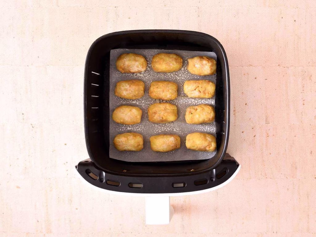 Tater tots are placed in an air fryer basket lined with parchment paper.