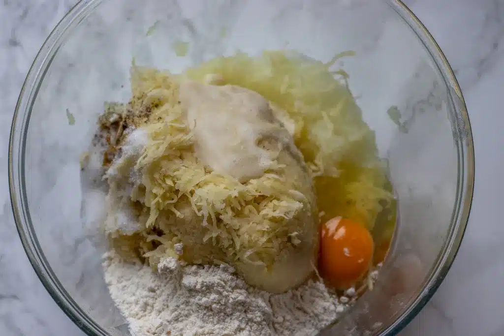 grated onions, potatoes, egg, flour, and seasoning are placed in a bowl