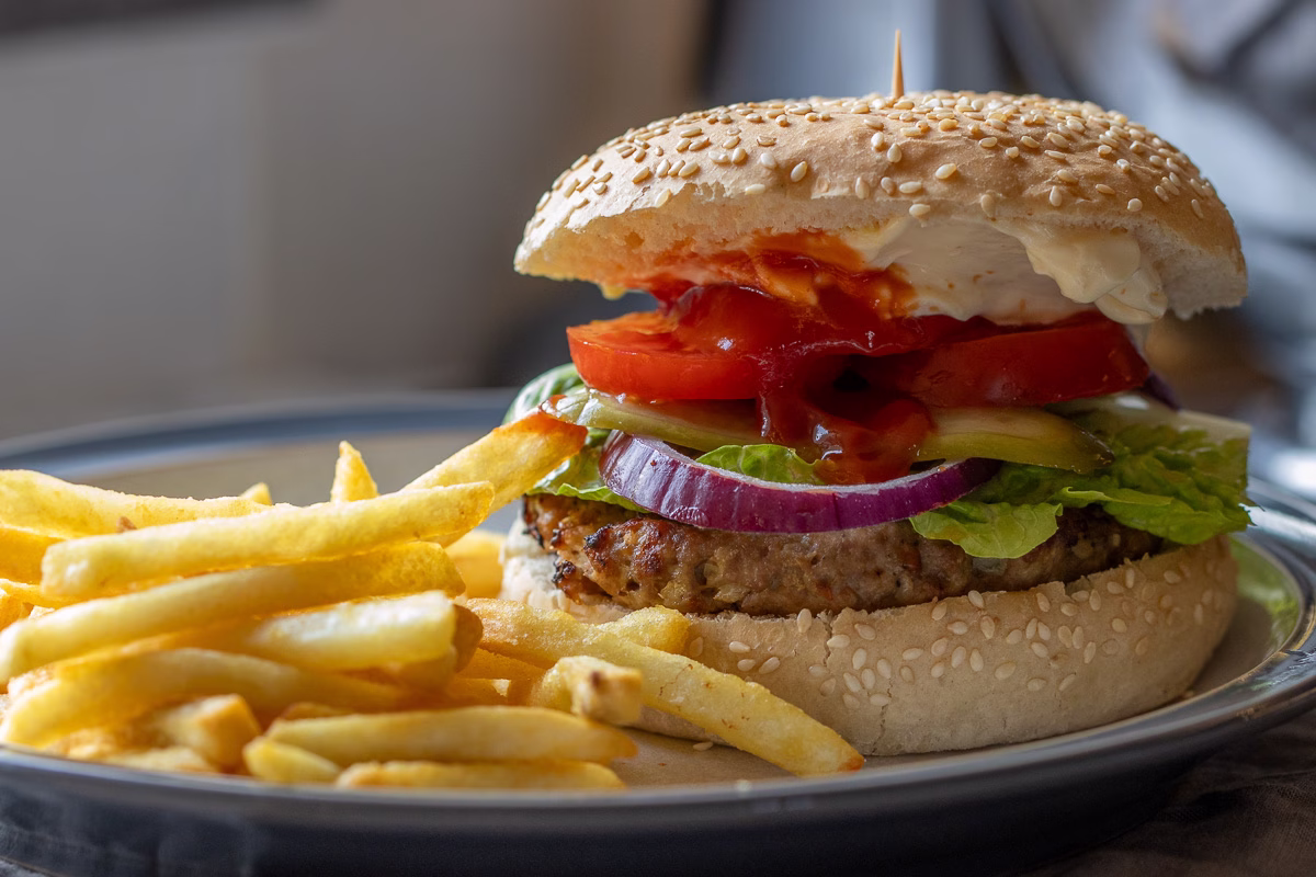 Turkey burger patty placed in a burger bun with lettuce, red onion, tomatoes, and pickles.