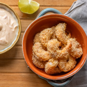 Golden air fryer panko shrimp in an orange bowl on a wooden board.