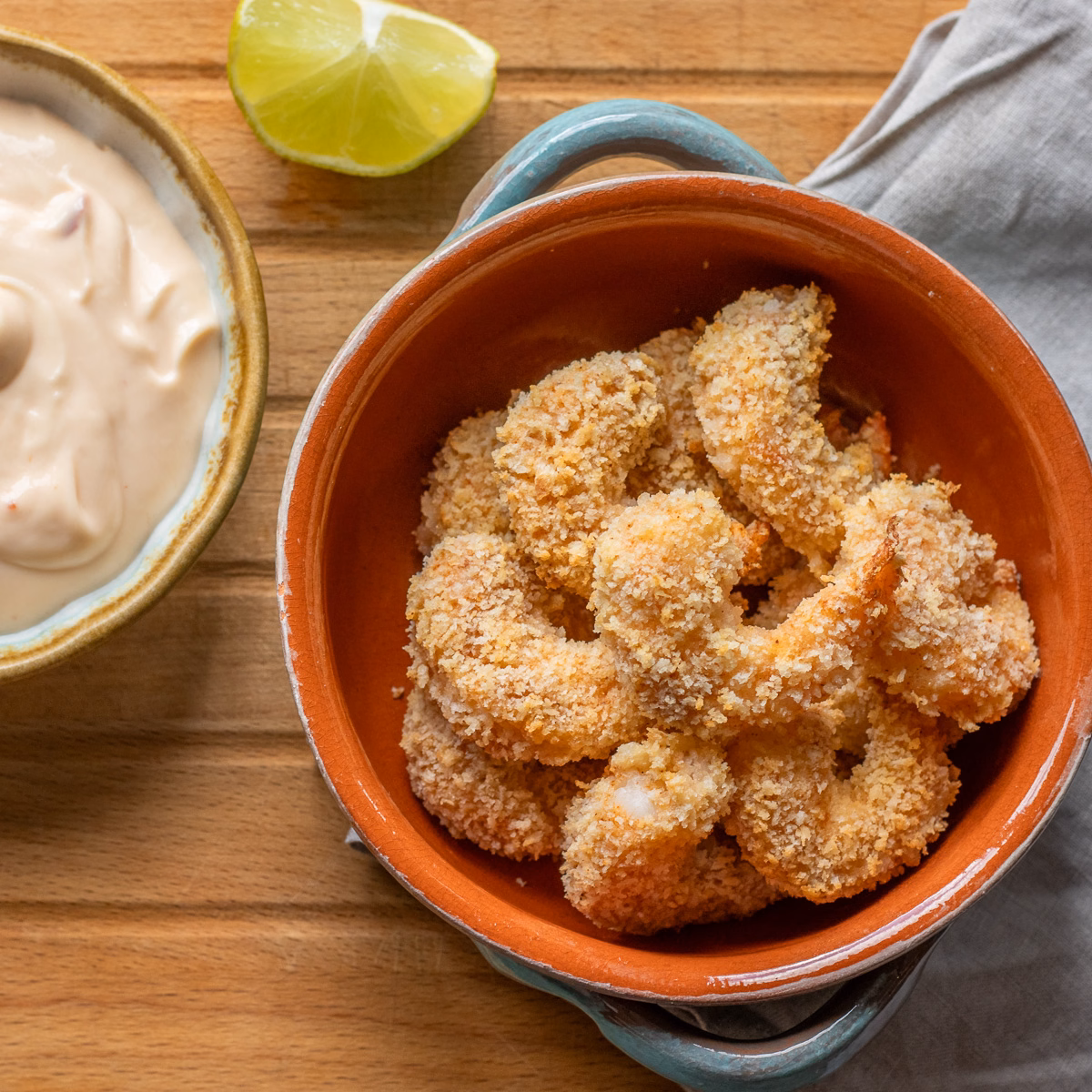 Golden air fryer panko shrimp in an orange bowl on a wooden board.